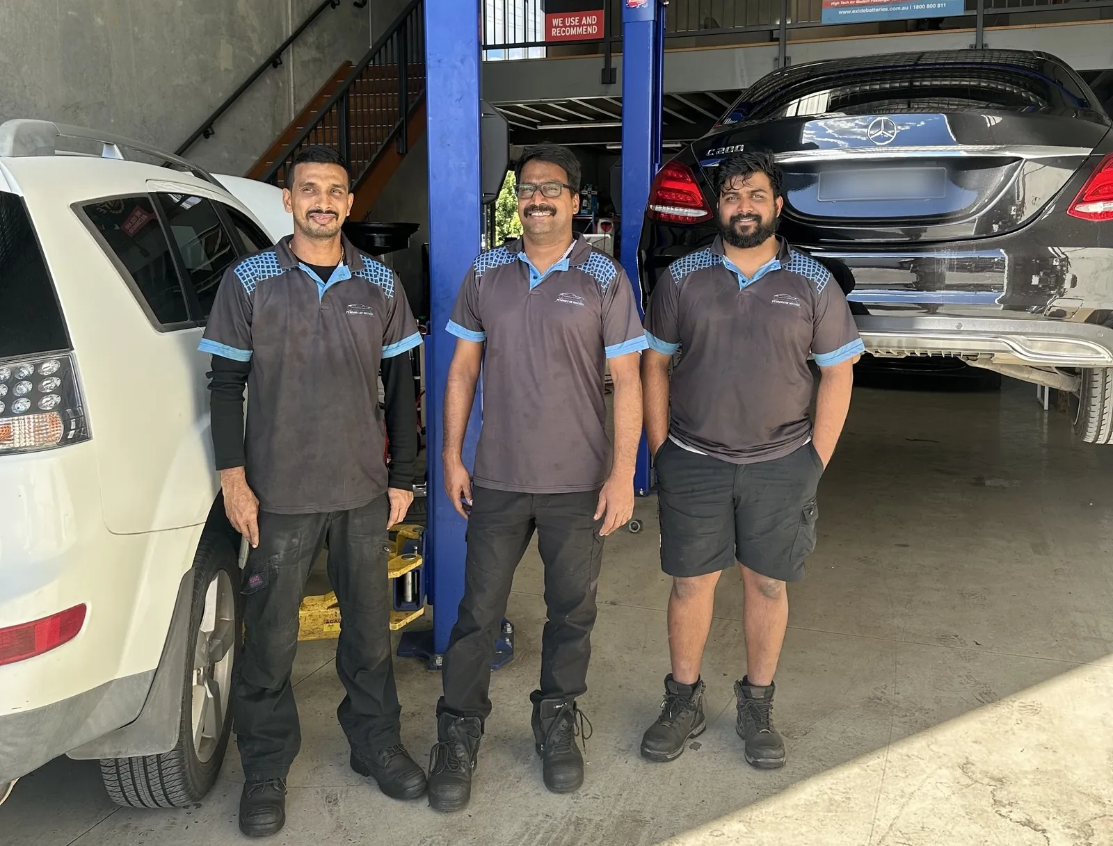The Peninsular Motors technicians in branded polos on the workshop floor at Crestmead, a Mercedes-Benz C 200 raised on the hoist behind them
